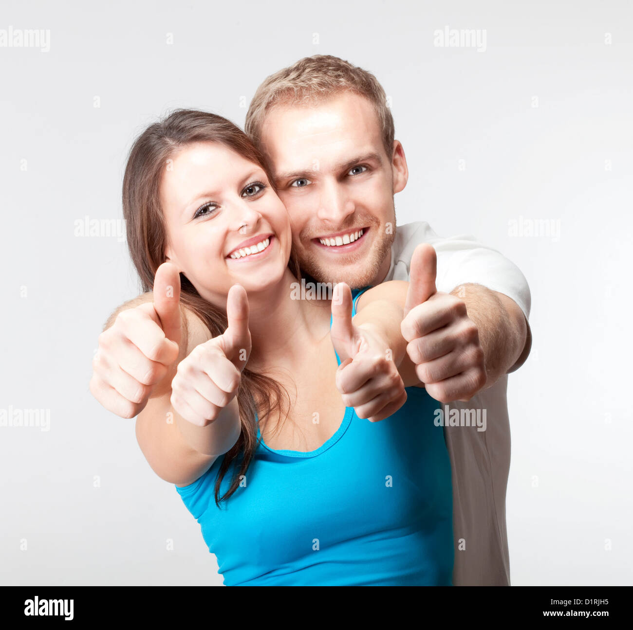 junges Paar zeigt beide Daumen nach oben lächelnd - isoliert auf grau Stockfoto