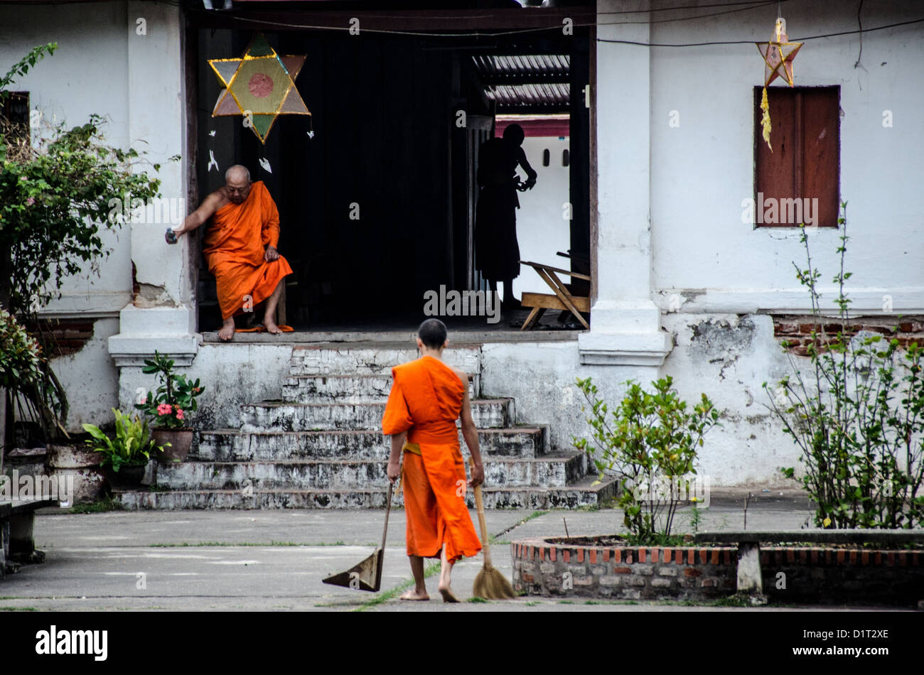 Buddhistische Mönche Reinigungskloster Luang Prabang Laos // LUANG PRABANG, Laos — buddhistische Mönche und Novizen in hellen Safrangewändern erfüllen ihre frühen Reinigungsaufgaben vor einem Kloster in Luang Prabang. Die tägliche Pflege des Klostergeländes ist ein integraler Bestandteil des Klosterlebens und der spirituellen Praxis im Theravada-Buddhismus. Luang Prabang ist ein wichtiges Zentrum buddhistischer Lehre und Praxis in Laos und Heimat zahlreicher aktiver Klöster und Tempel. Die Klostergemeinde der Stadt folgt traditionellen Routinen, die seit Jahrhunderten gepflegt wurden, einschließlich Gemeindearbeit und Medi Stockfoto
