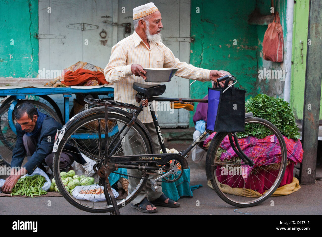 Ein indischer Mann in traditioneller Kleidung sammelt einige Gemüse vom Markt mit seinem Fahrrad in Udaipur, Rajasthan Indien Stockfoto