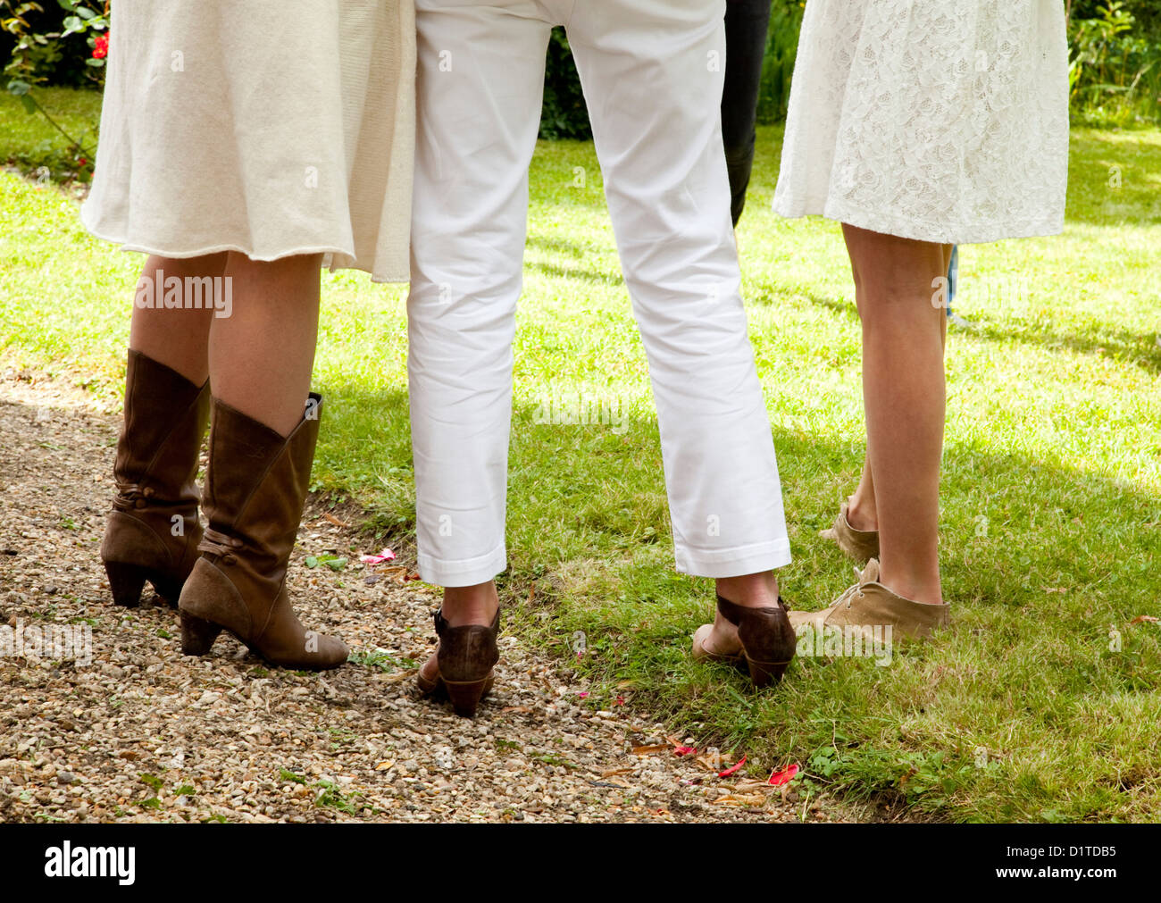 Drei Gruppen von Frauen Beine stehen in weißer Kleidung und braune Schuhe zusammen auf dem grünen Rasen in einem Garten im Sommer. Stockfoto