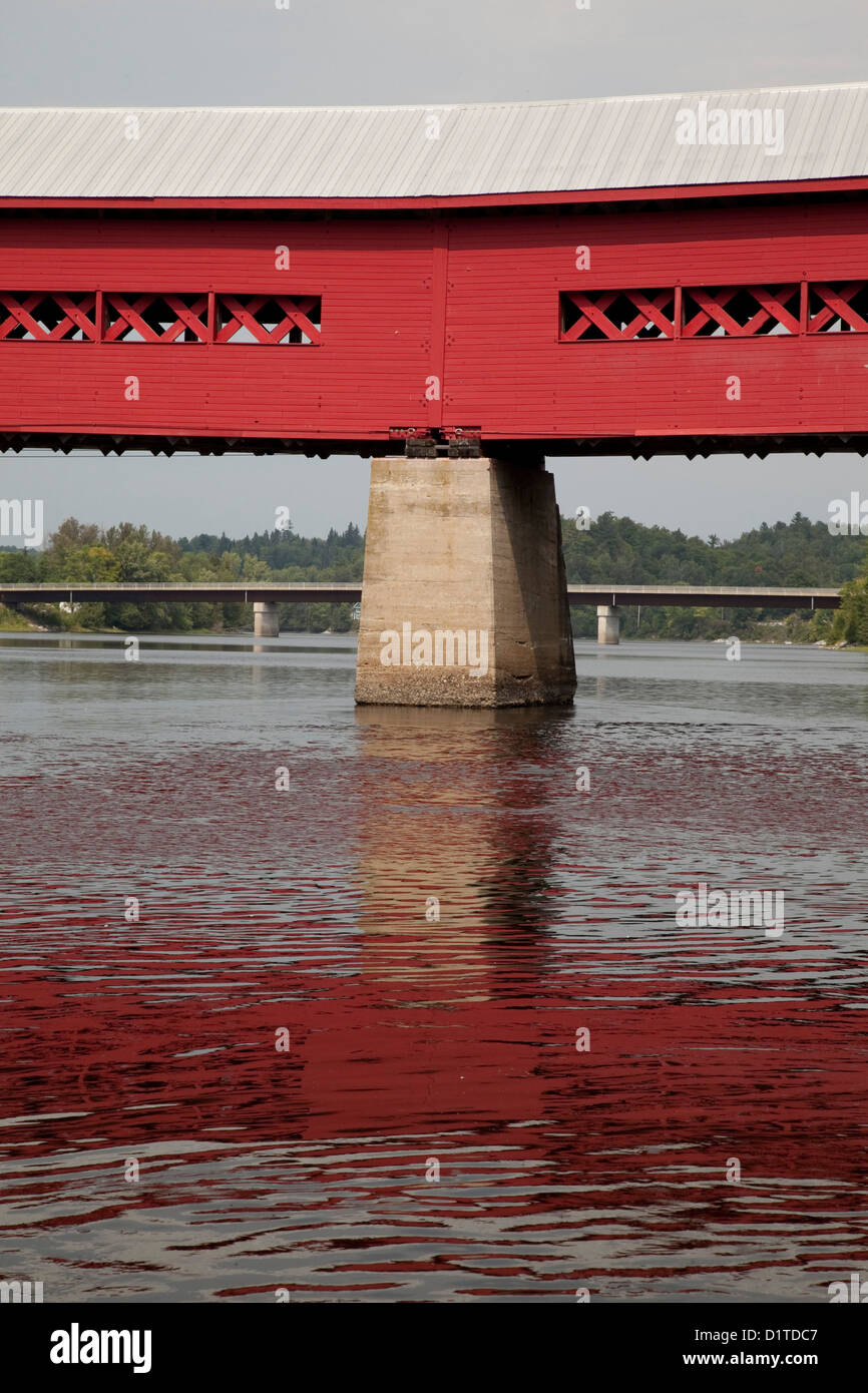 Ein vertikales Bild eine rote hölzerne Fußgängerbrücke über den Ottawa-Fluss, die Spiegelung im Wasser. Stockfoto