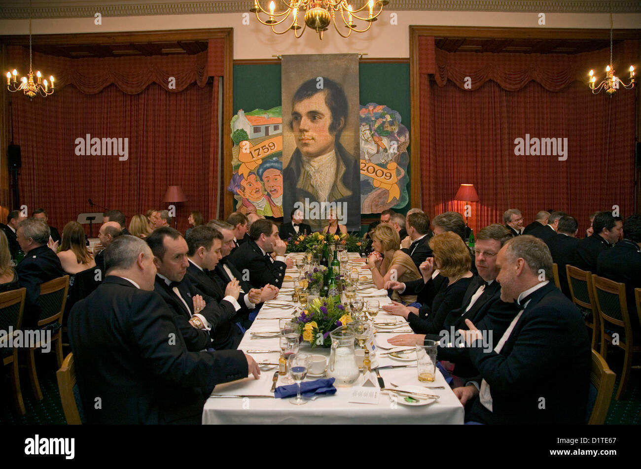 Gäste sitzen für eine Burns Supper mit einem Wandbild Darstellung der 200. Geburtstag von Robert Burns Stockfoto