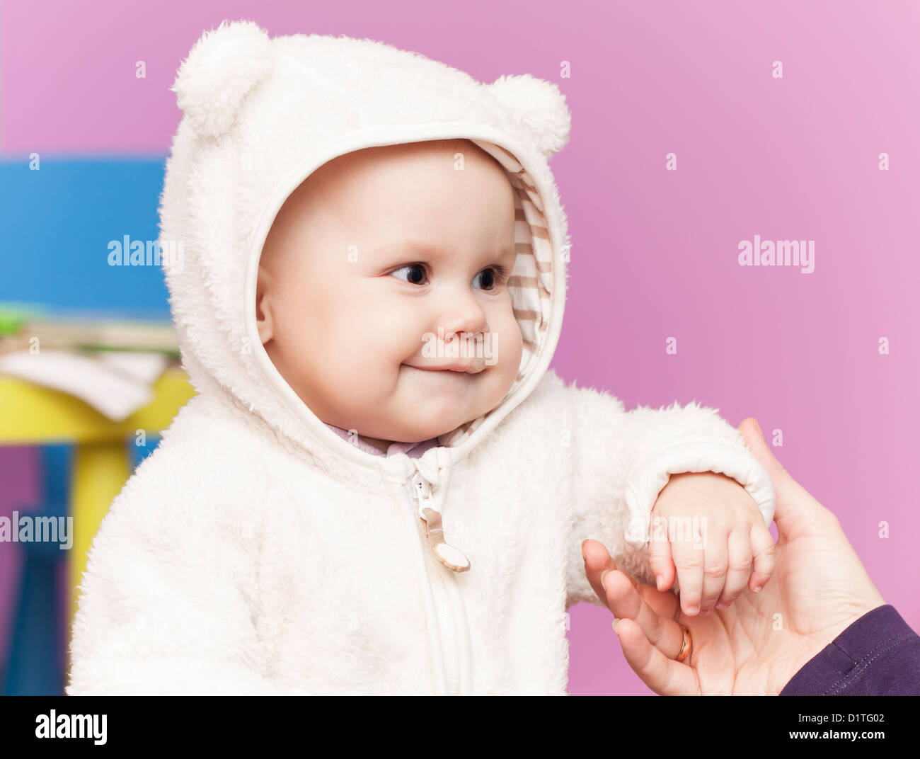 kleines Baby in weißer Bär Kostüm Lächeln und halten Mütter hand Stockfoto