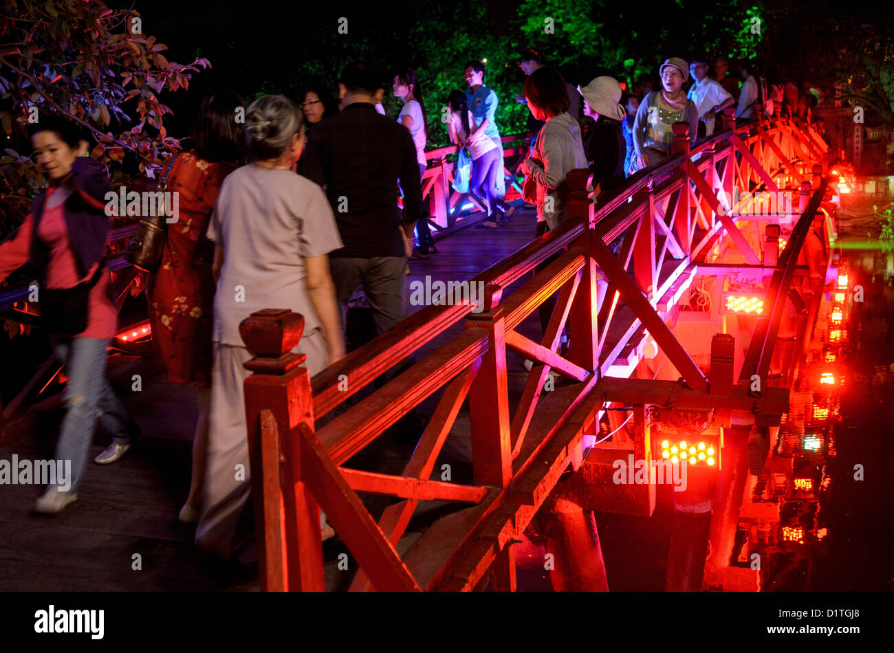 HANOI, Vietnam – Touristen besuchen die Huc-Brücke (Morgensonnenbrücke) bei Nacht. Die rot gestrichene Holzbrücke verbindet das Nordufer des Sees mit der Jade Island und dem Tempel des Jade Mountain (Ngoc Son Temple). Stockfoto