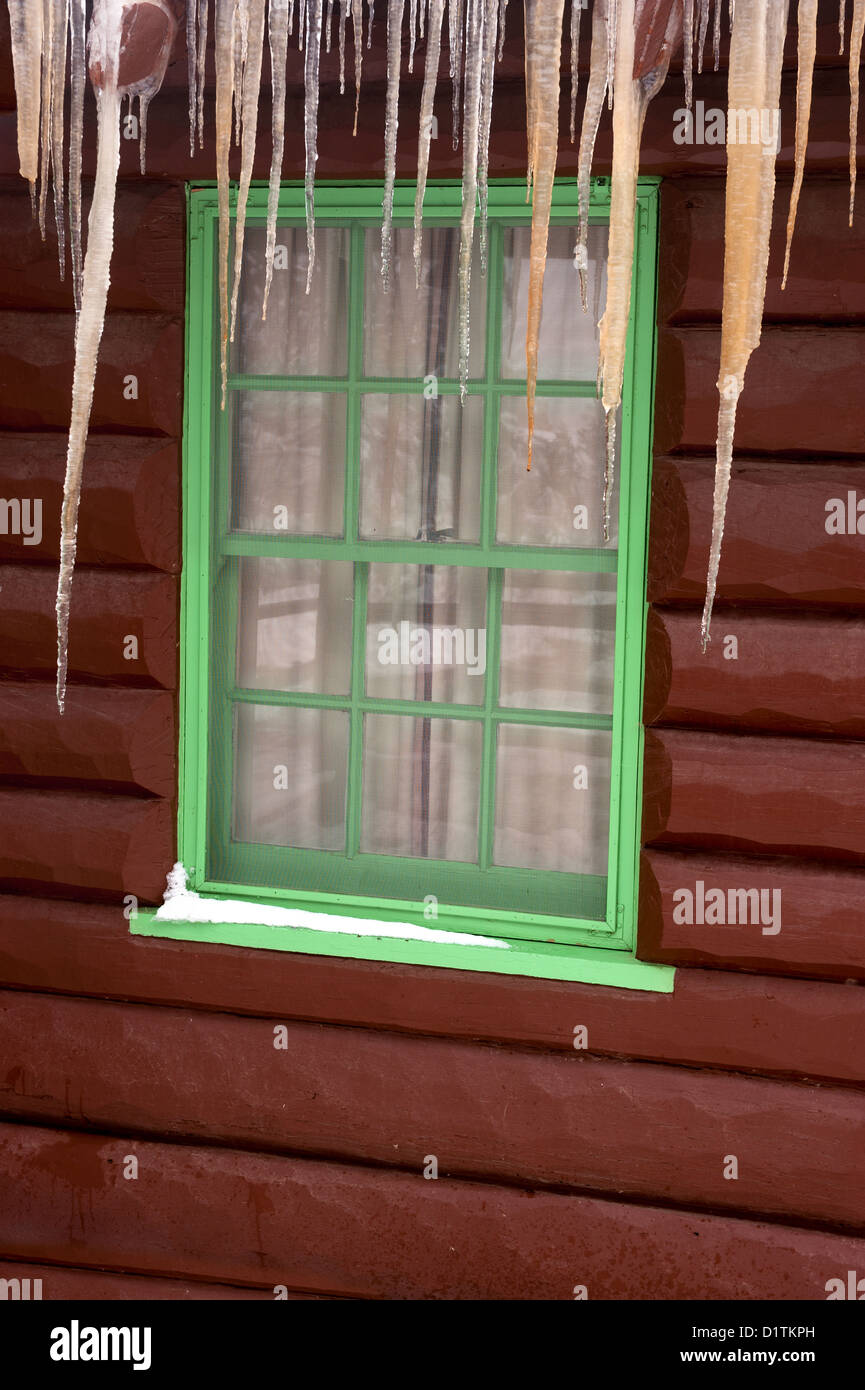 Nahaufnahme von einem Blockhaus-Fenster mit Eiszapfen hängen von der Decke über dem Fenster Stockfoto