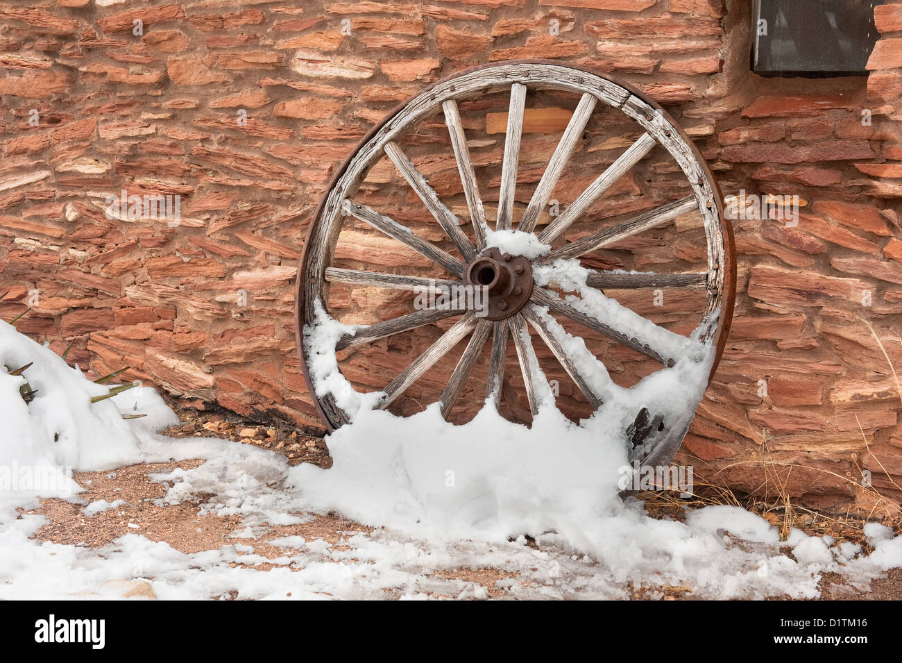 Eine alte, antike Wagenrad mit Schnee bedeckt ruht einer Ranch Anlage Wand. Stockfoto