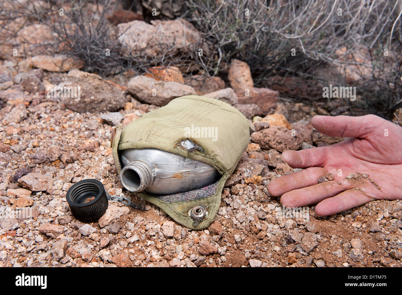 Ein Wanderer in der extremen Wildnis erliegt Dehydrierung während in der abgelegenen Wüste, angezeigt durch eine alte, leere Kantine. Stockfoto