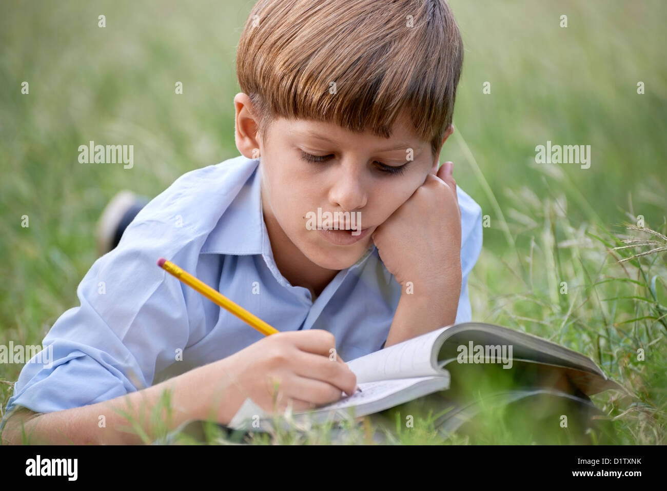 Jugend und Bildung, Schulkind, Hausaufgaben, Festlegung auf dem Rasen im Park und studieren mit Buch. Mittlere Aufnahme Stockfoto