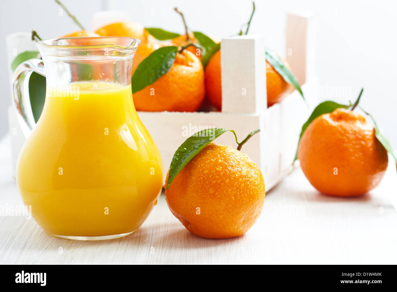 Orangensaft im Krug und Mandarinen mit Blätter in Holzkiste Stockfoto