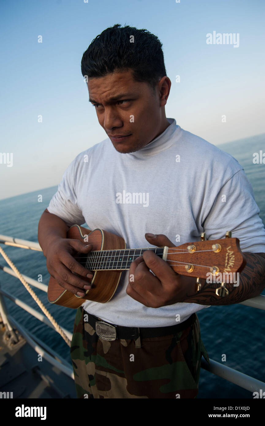 Luftfahrt-Maschinist Mate 3. Klasse Jerome Roberts von Rapid City, S.D., spielt eine Ukulele bei einem Stahl Strand-Picknick auf dem Vorschiff der Ticonderoga-Klasse geführte Flugkörper Kreuzer USS Mobile Bay (CG-53). Mobile Bay mit der John C. Stennis Strike Group in den USA bereitgestellt wird 5. Flotte Aufgabengebiet Durchführung von maritimer Sicherheitsoperationen, Theater Sicherheitsbemühungen Zusammenarbeit und Unterstützung Missionen für Operation Enduring Freedom(Jan. 7, 2013). (Foto: U.S. Navy Mass Communication Specialist 2. Klasse Armando Gonzales/freigegeben) Stockfoto