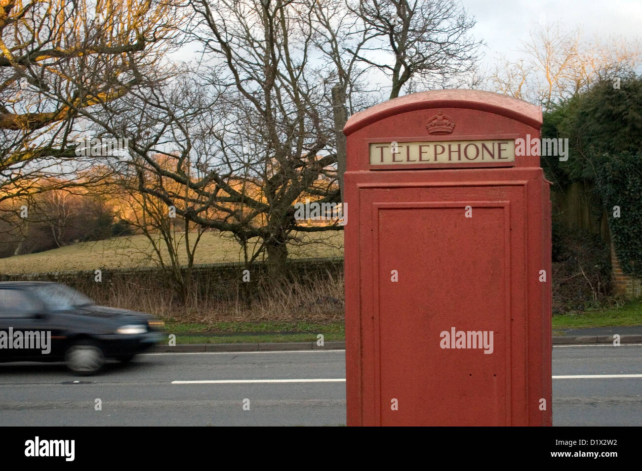Ein Auto, ein am Straßenrand traditionellen roten britischen Phonebox vorbei. Stockfoto