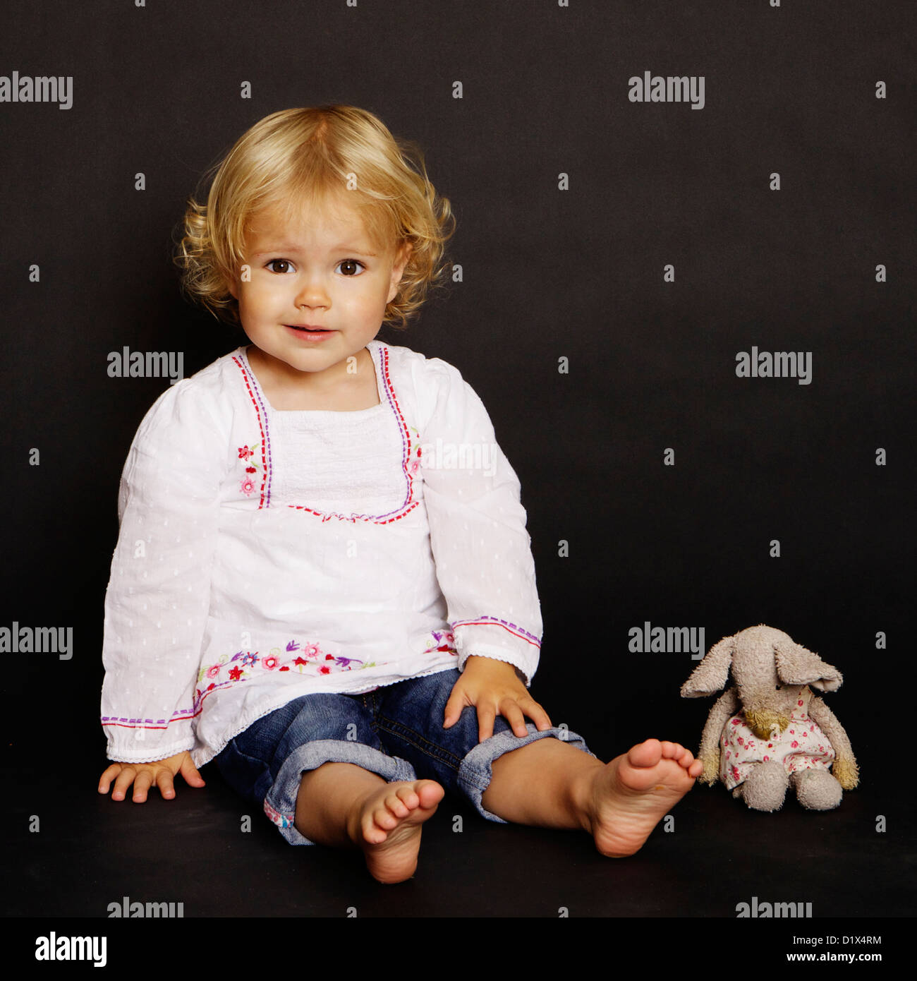 Zwei Jahre alten Säugling Blondine in weißen Hemd und Jeans auf schwarzem Hintergrund Stockfoto