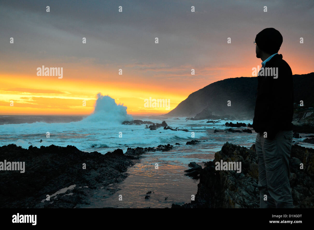 Mann, Blick auf Sonne und dramatische Wellen an der Küste Südafrikas einstellen Stockfoto