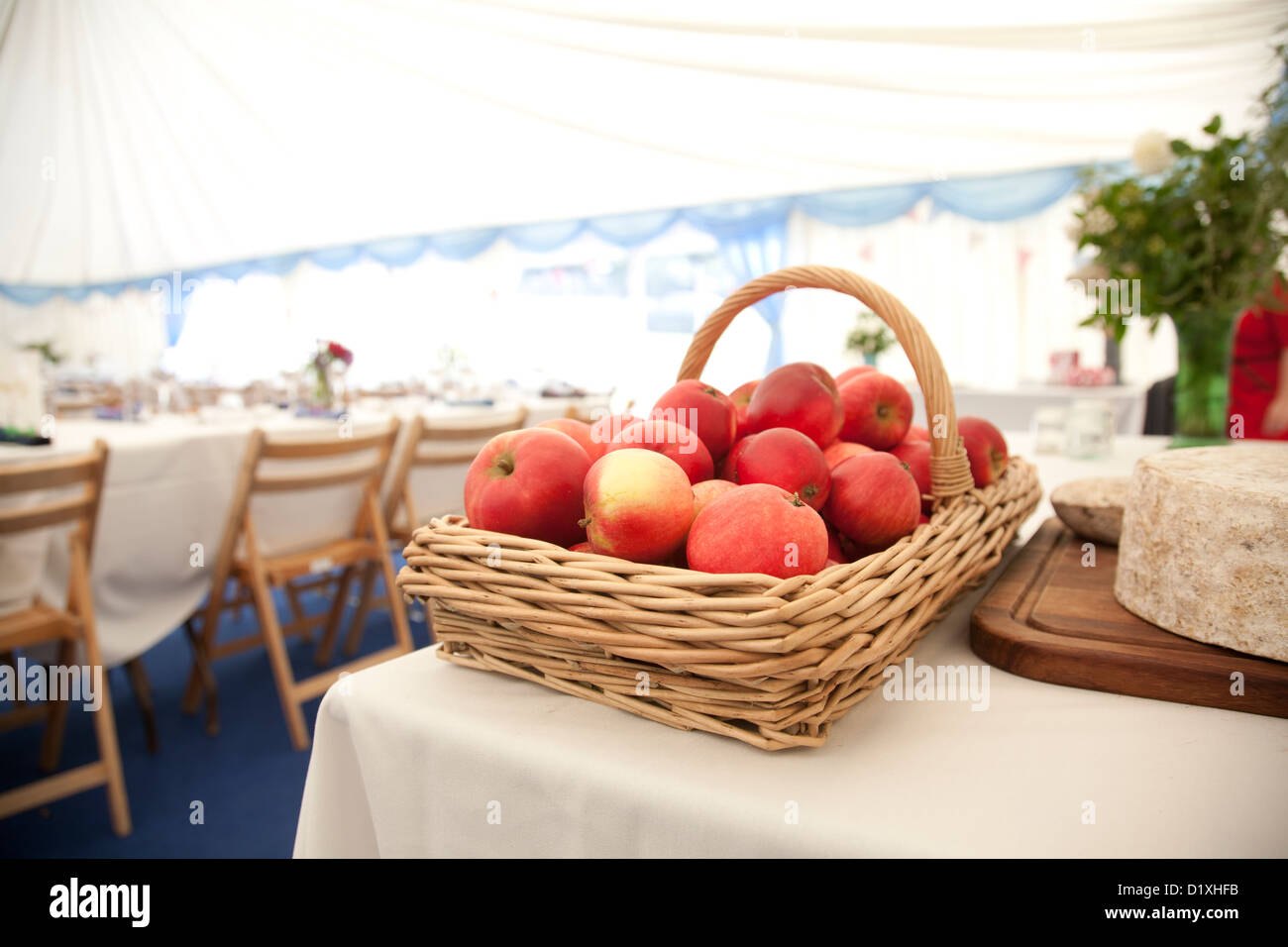 Korb mit roten Äpfel auf einem Tisch neben Käse mit Tischen und Stühlen für eine Hochzeitsfeier in einem Zelt im Hintergrund festlegen Stockfoto