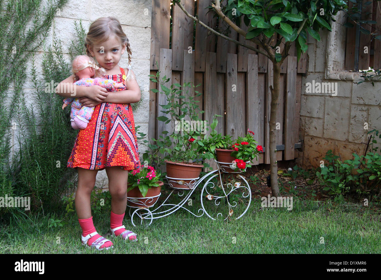 Überqueren Sie weiblichen Kleinkind mit seiner Puppe in einem Garten Model-release Stockfoto