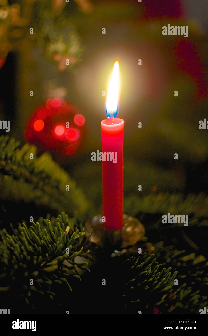 Brennende, rote Kerze am Weihnachtsbaum. Weihnachtskugel im Hintergrund. Stockfoto