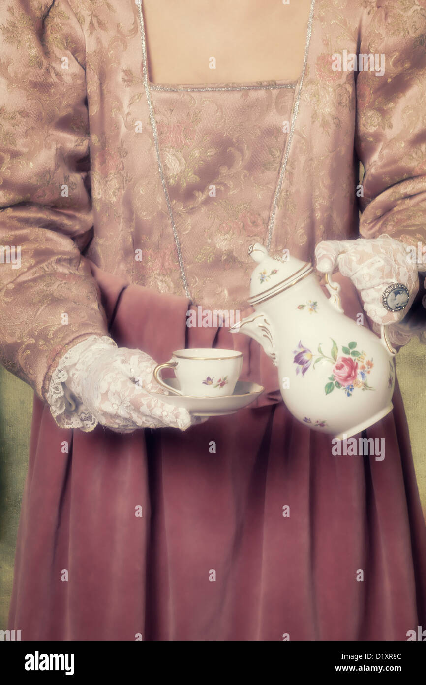 eine Frau in einem Zeitraum Kleid ist Kaffee in eine Tasse Gießen. Stockfoto