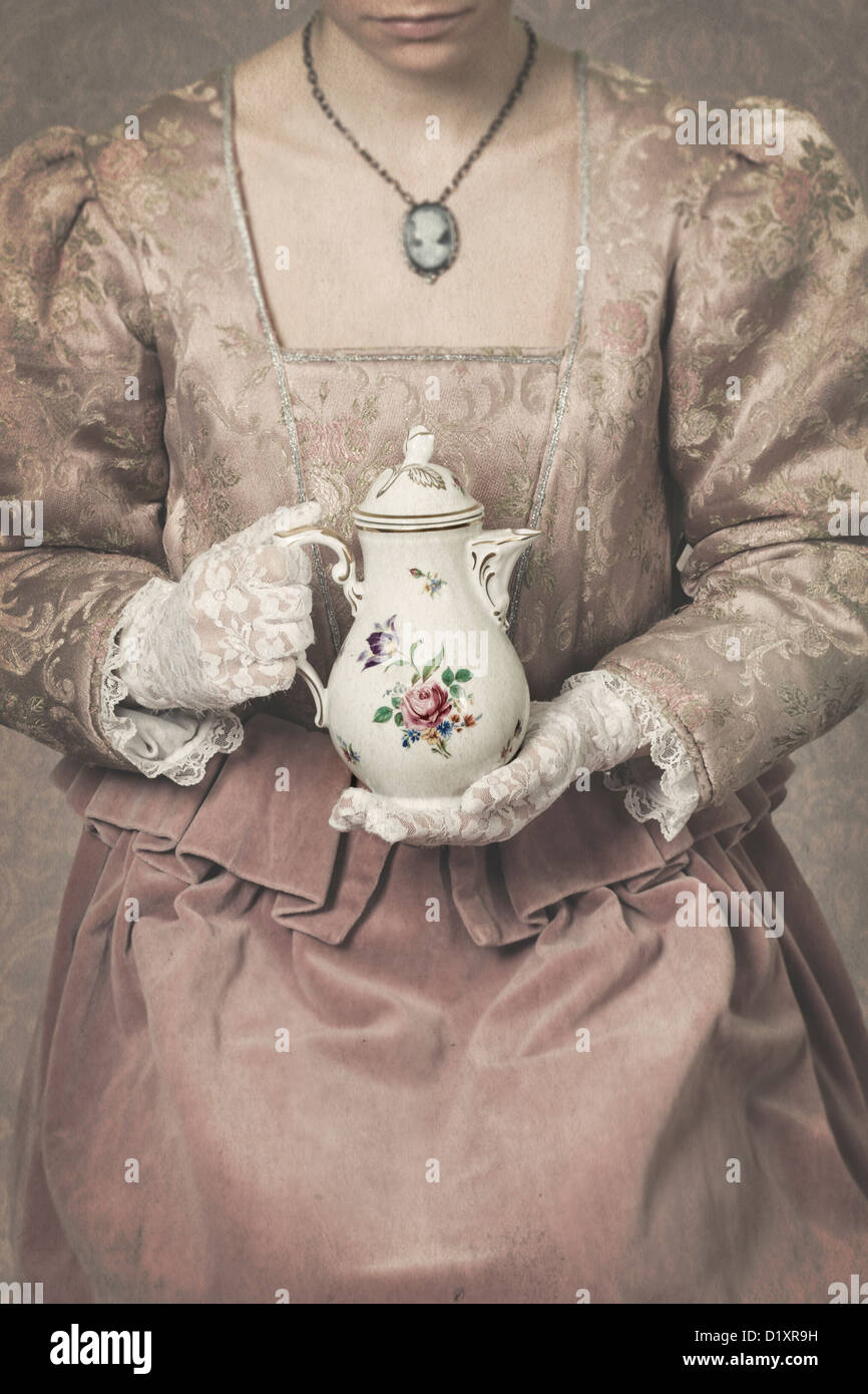 eine Frau in einem Zeitraum Kleid hält eine Kaffeekanne Stockfoto