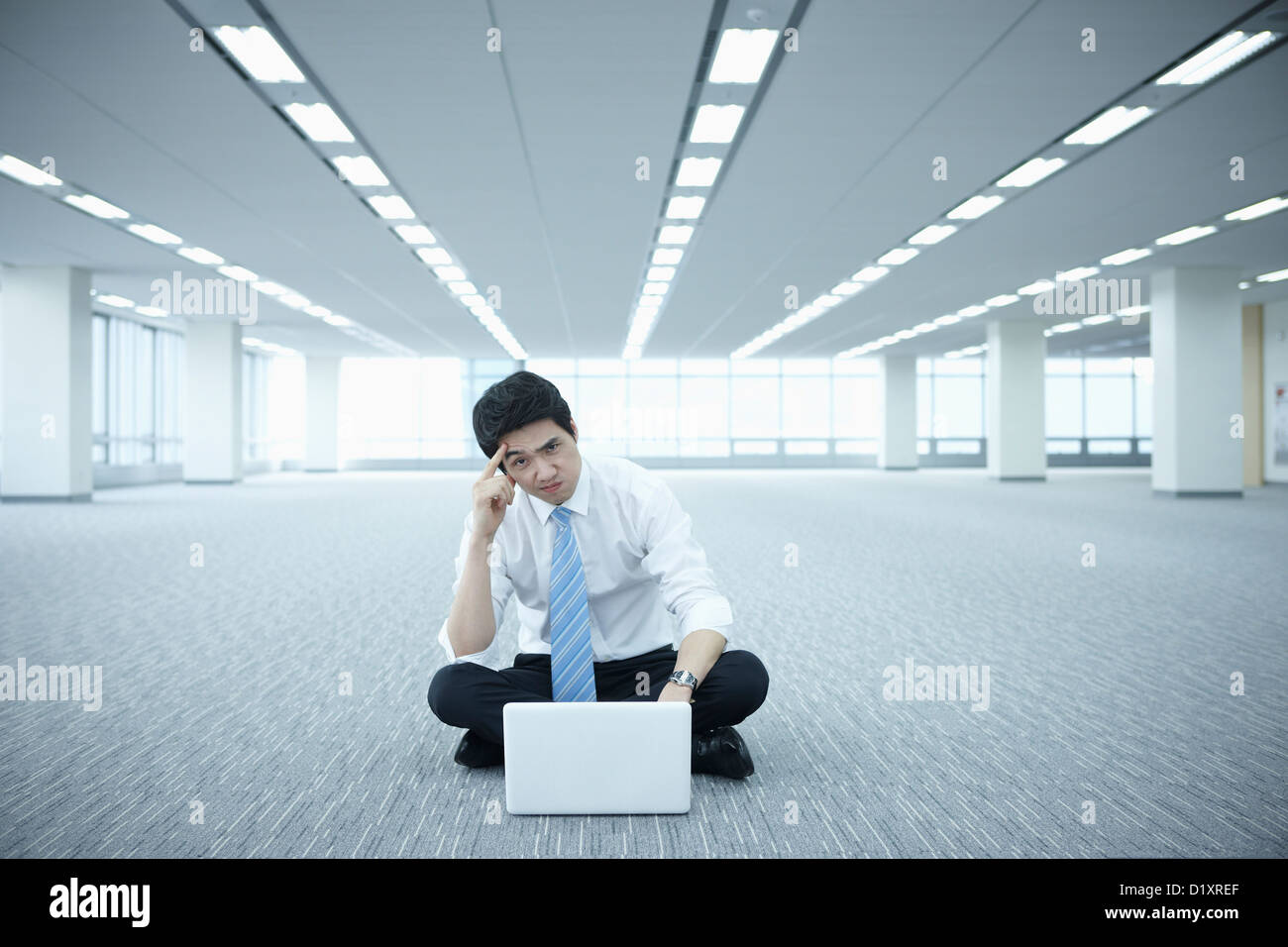 ein Geschäftsmann mit Laptop auf dem Boden von einem leeren Raum Stockfoto