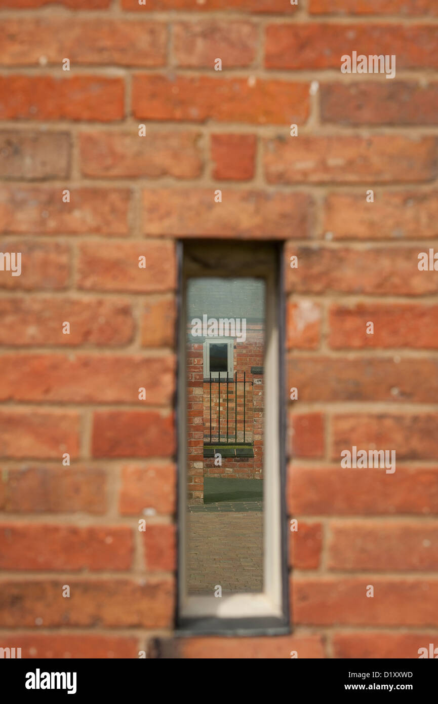 Nahaufnahme eines schmalen Fensters spiegelt den Gartenbereich außerhalb einer neu umgebauten Scheune in der englischen Landschaft. Stockfoto