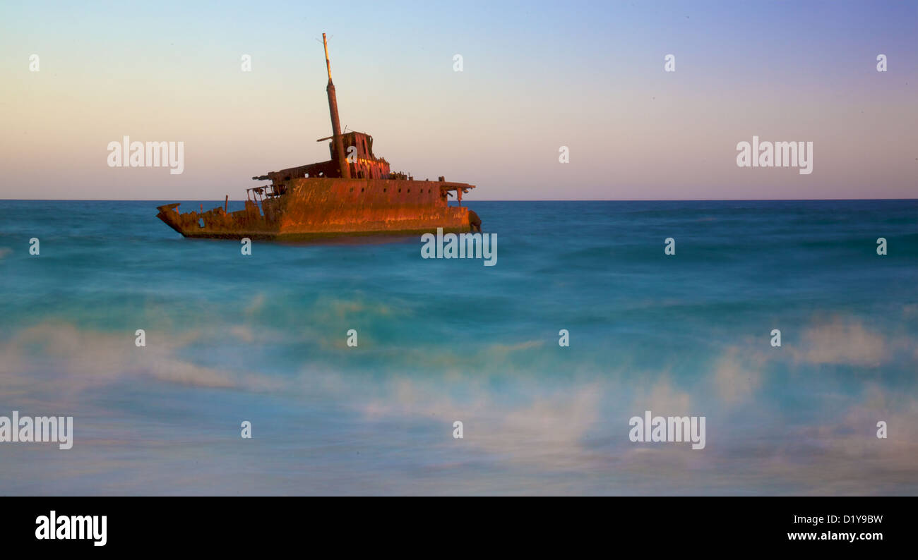 ein Schiffswrack am Strand mit einem Baumstamm im Vordergrund Stockfoto