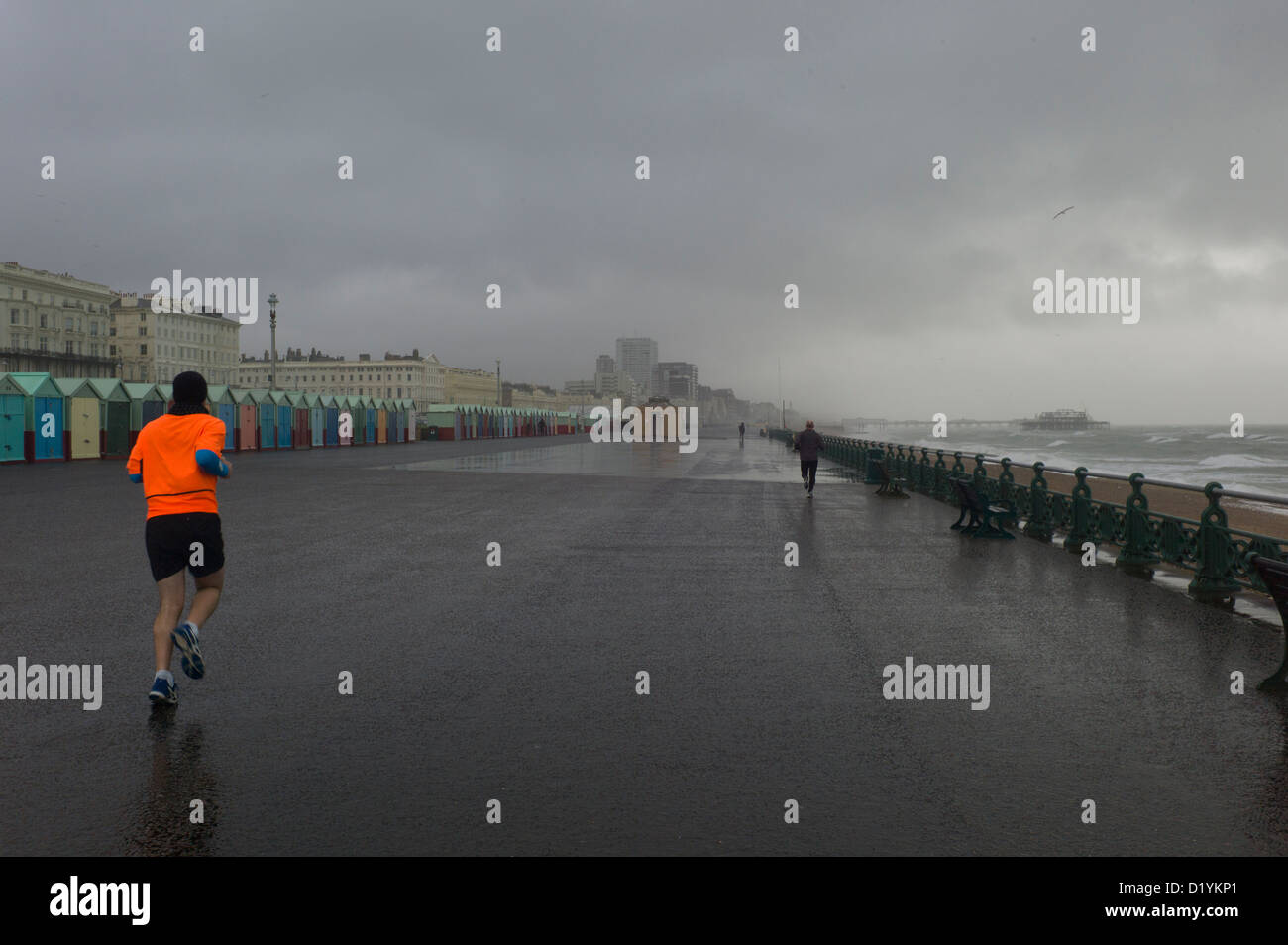 Jogger in stürmischen Himmel, Regen, Strandhütten, Brighton seafront Stockfoto