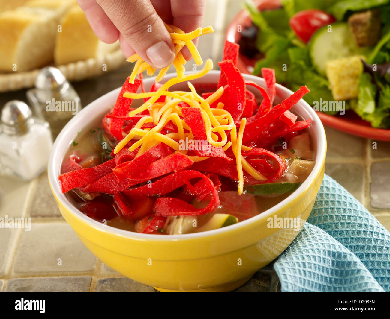 Tortilla Suppe mit einer Hand streuen, Käse und einem Beilagensalat Stockfoto