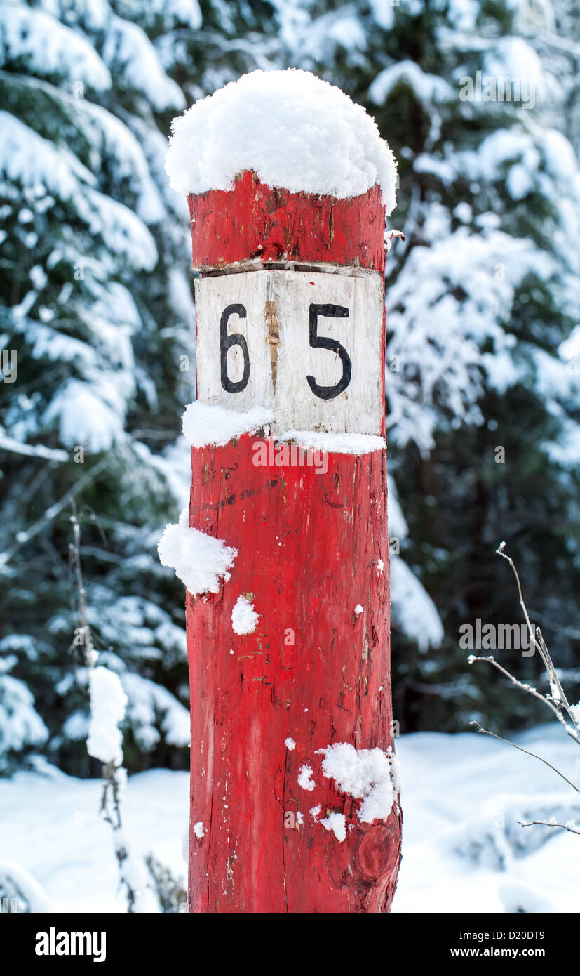 Alten verwitterten roten Holz Kilometer Schild mit Schnee auf dem Forstweg Stockfoto