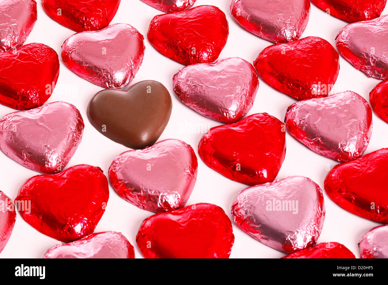 Schokoladenherzen in rot und Pick-Folie-Wrapper auf einem weißen Hintergrund mit einem ausgepackten Herzen in der Gruppe. Stockfoto