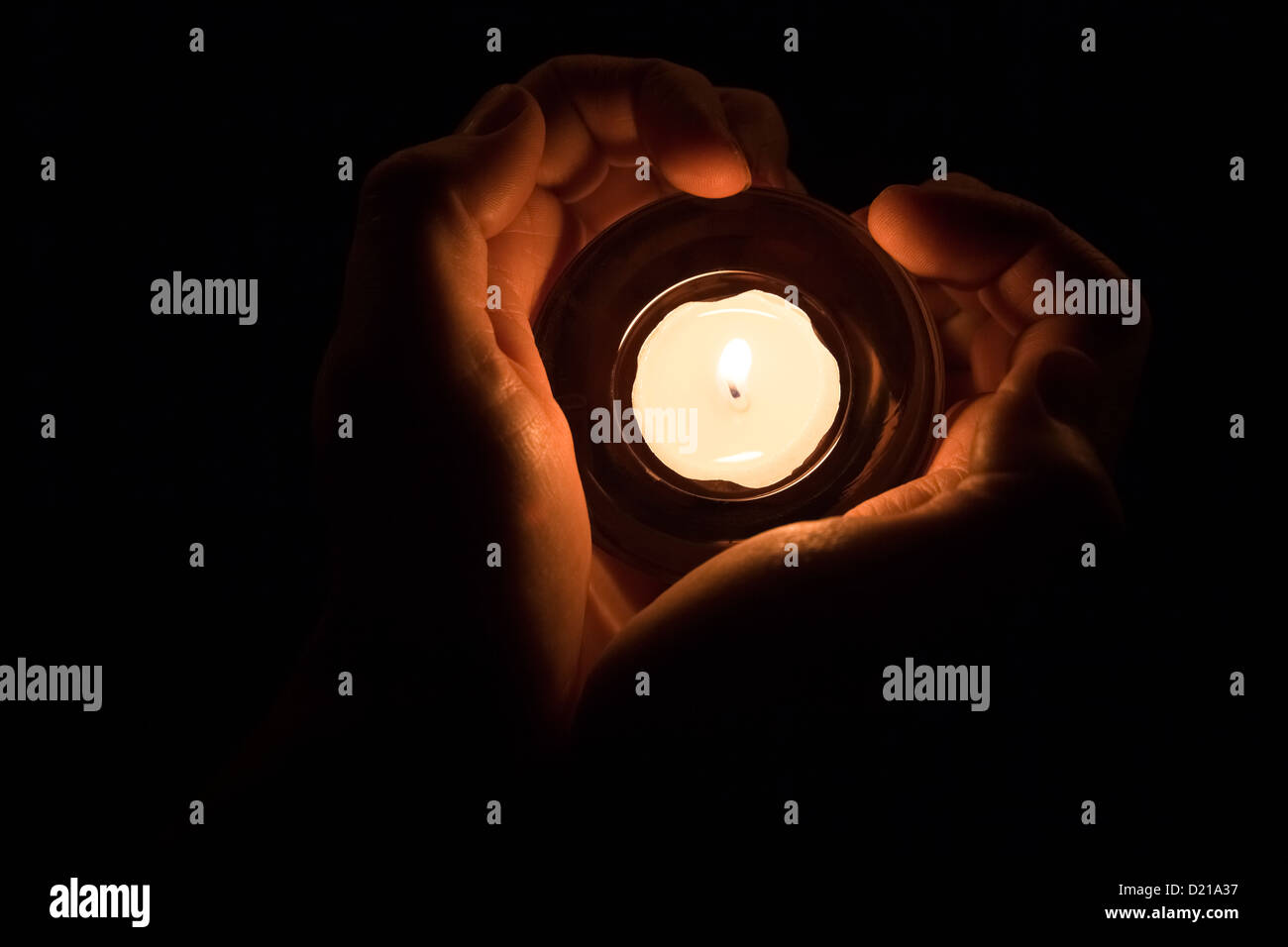 Hände in der Form eines Herzens um eine brennende Kerze. Stockfoto