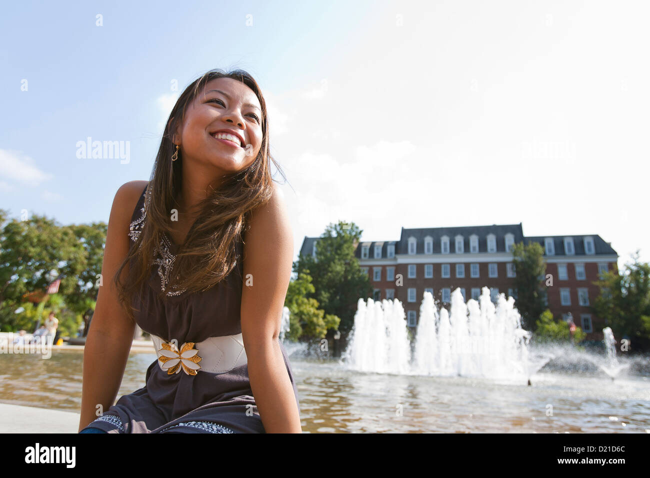 Junge asiatische Frau sitzt am Rand der öffentlichen Brunnen Stockfoto