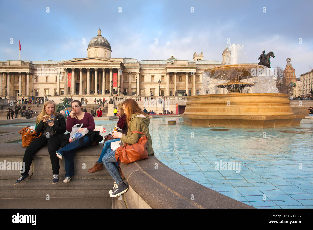 Touristen sitzen am Rande der Brunnen am Trafalgar Square mit der Nationalgalerie im Hintergrund London England UK Stockfoto