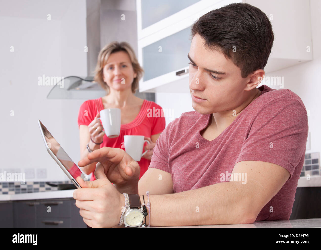 Junger Mann mit einem digitalen Tablet-Bildschirm oder Monitor zu betrachten. Befindet sich in einer modernen Küche eine Frau mit zwei Tassen Lächeln Stockfoto