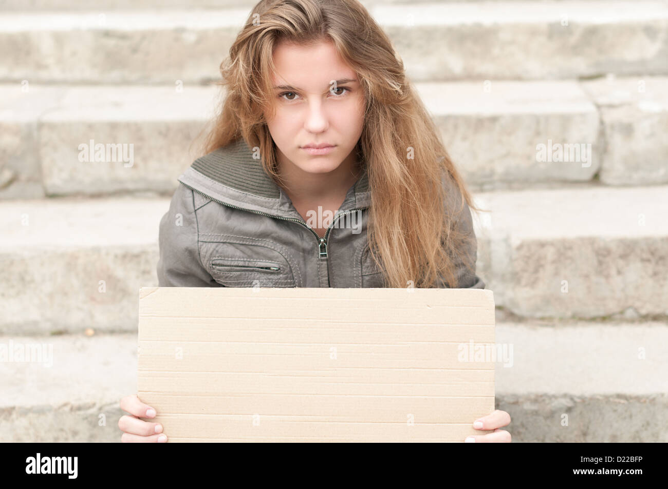 Teenager-Mädchen sitzen im Freien auf graue Steinstufen mit leeren Pappschild in ihren Händen verlassen. Junges Mädchen schauen traurig und de Stockfoto