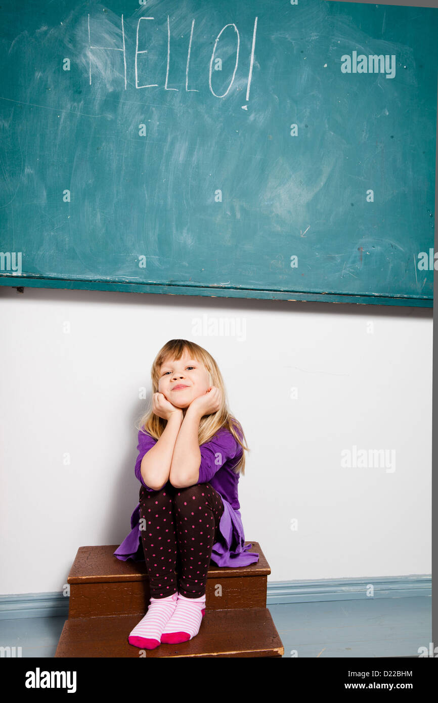 Studioportrait von lächelnden jungen Mädchen sitzen im Klassenzimmer mit Wort Hallo auf Tafel geschrieben Stockfoto