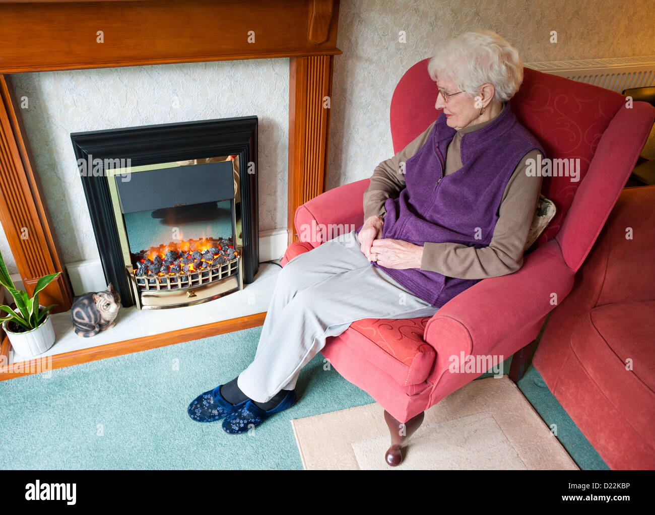 Eine ältere Frau sitzt am elektrischen Kamin. Stockfoto
