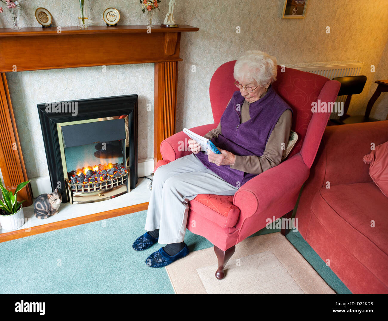 Eine alte Frau sitzt am elektrischen Kamin tun eine Kreuzworträtsel  Stockfotografie - Alamy