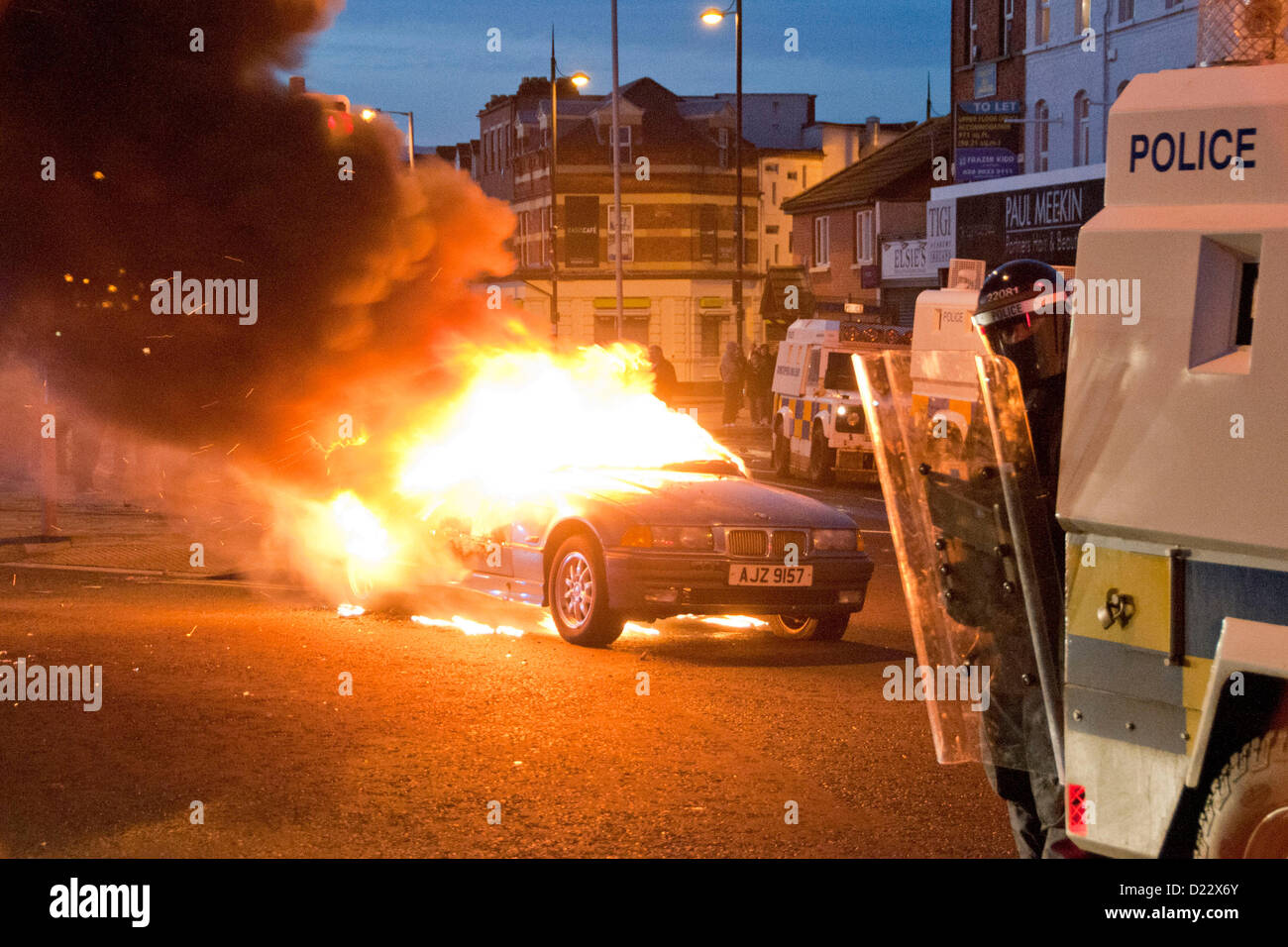 Belfast, UK. 01.12.13.  Ein Polizist in der Beersbridge Gegend blickt vom Cover der ein gepanzertes Fahrzeug, wie ein Auto im Hintergrund brennt. Ein Auto brennt in den Rücken als randalierende Pausen in Belfast Borough von Castlereagh...  © Pete Maclaine / Alamy Live News Stockfoto