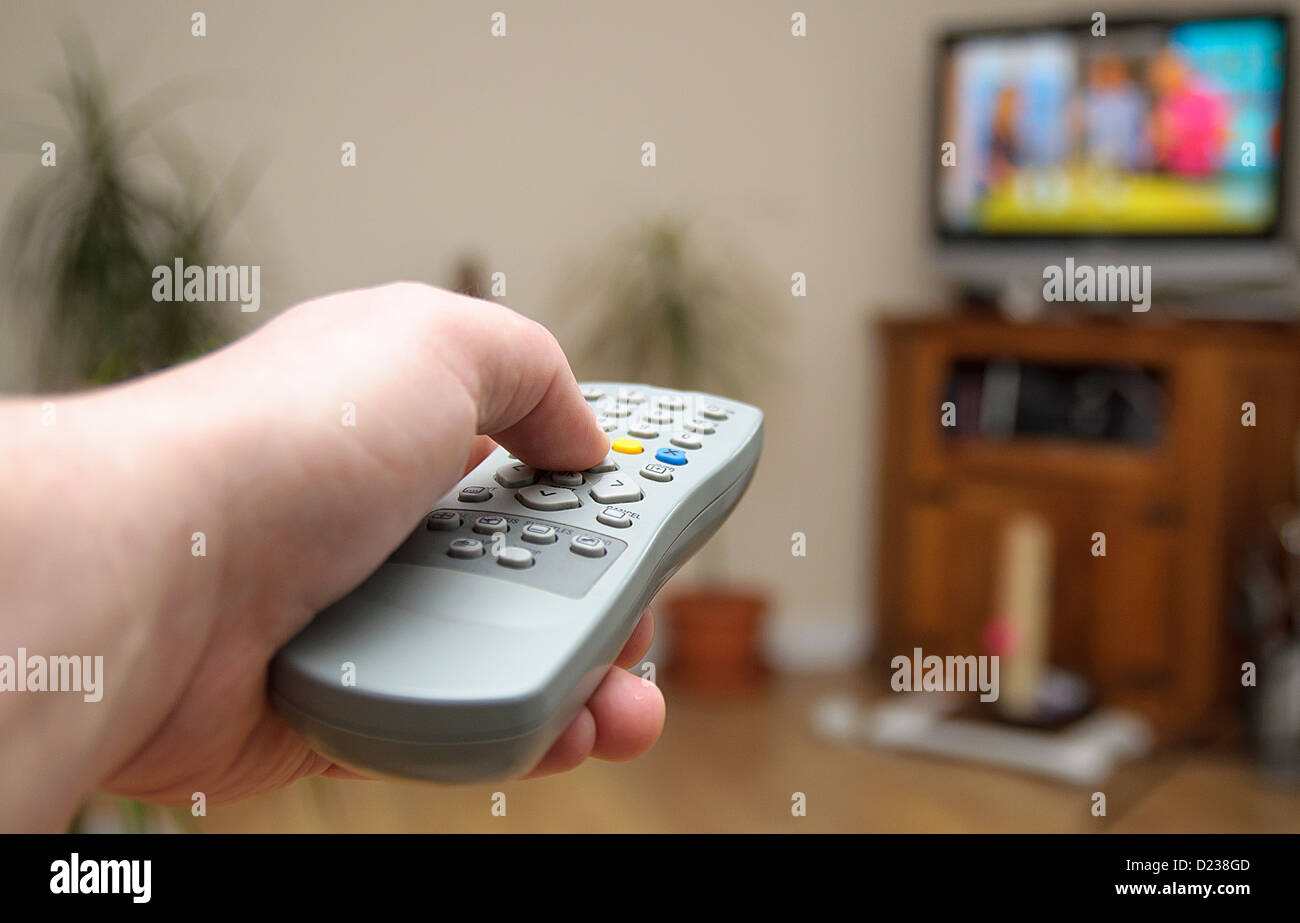 Eine Hand hält eine TV-Fernbedienung auf den Fernseher gerichtet. Stockfoto