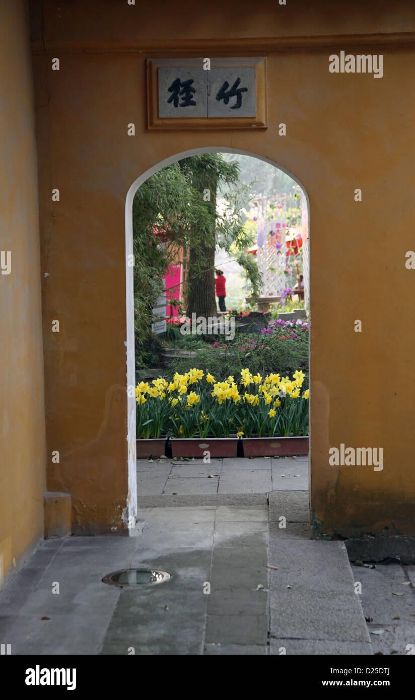 Es ist ein Foto von dem Eingangstor von einem alten alten chinesischen Tempel. Es ist in gelber Farbe und wir können sehen, Bäume und Blumen. Stockfoto