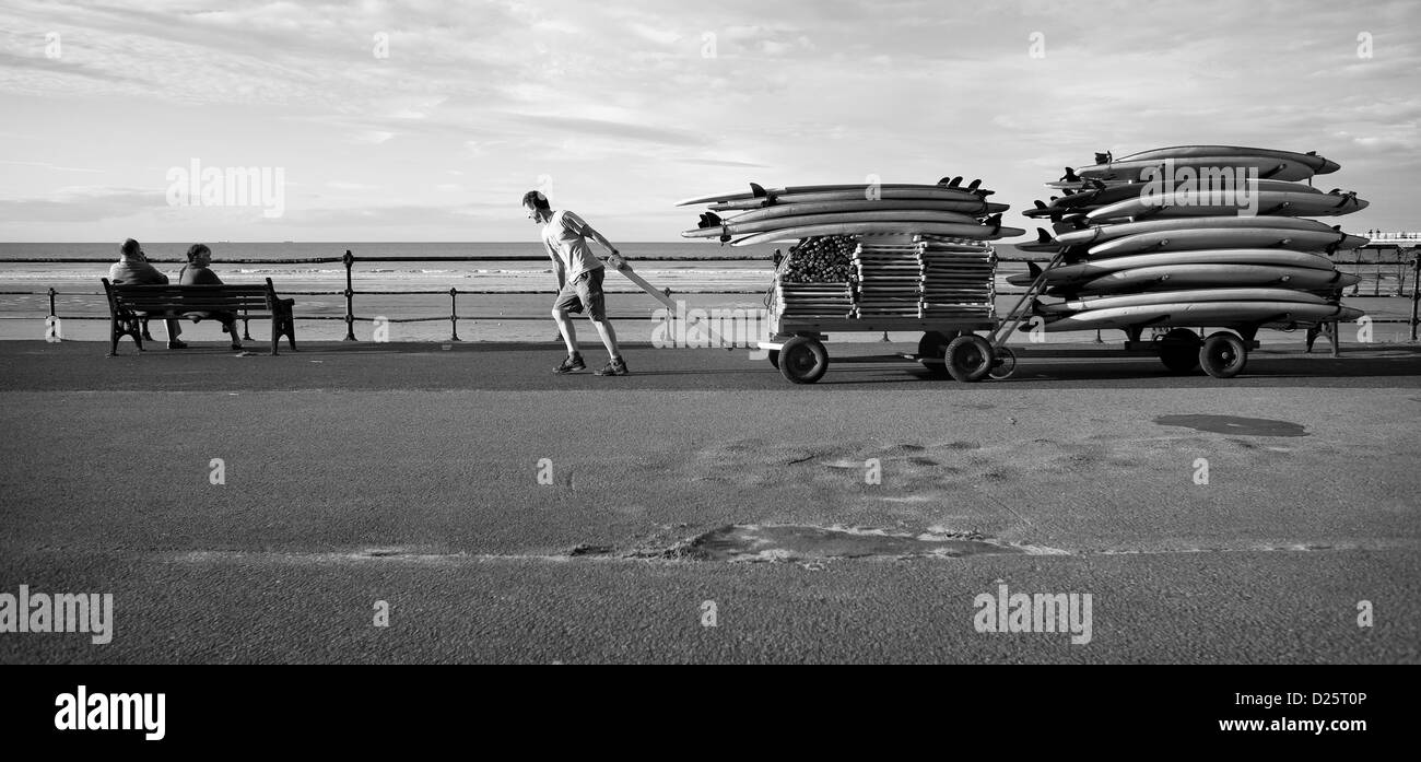 Surf Verleih Shop Besitzer Nick Noble zieht seinen Wagen beladen mit Surfbrettern entlang der unteren Promenade in Saltburn, Cleveland. Stockfoto