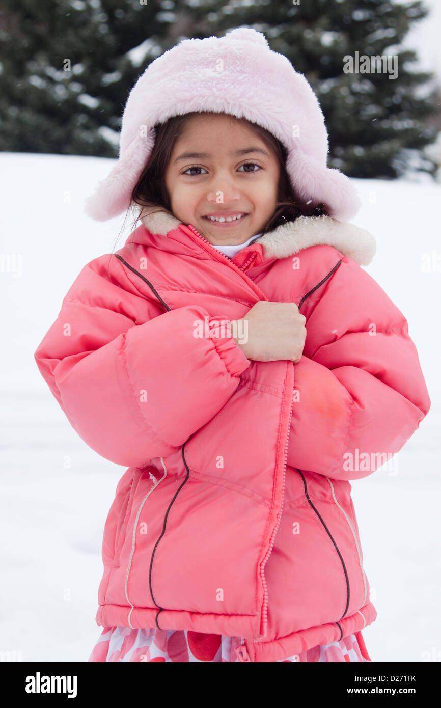 Ein schönes ostindischen Mädchen Kind Kupplungen an ihrer Jacke im Schnee. Stockfoto