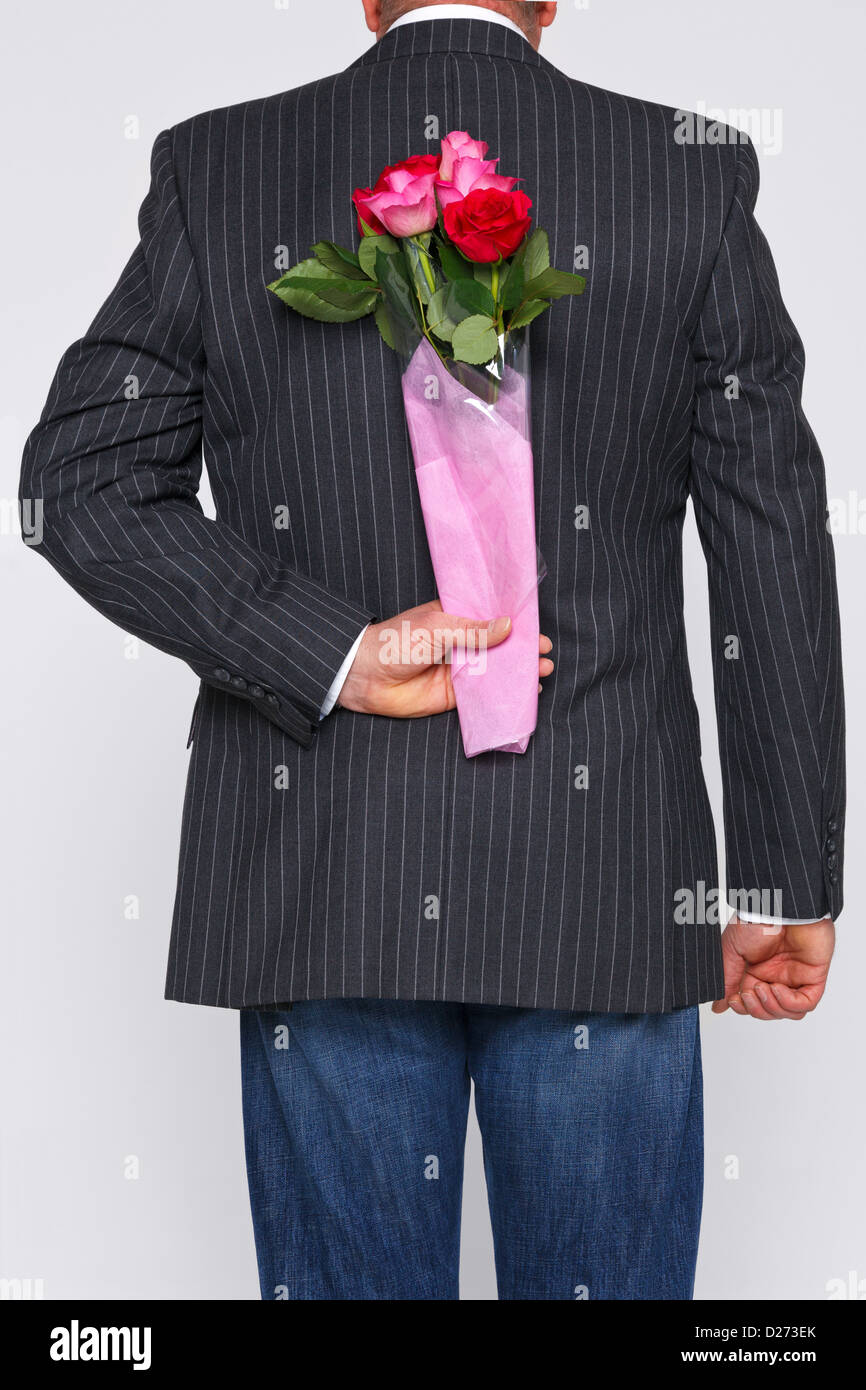 Ein Mann mit einem Rosenstrauß hinter seinem Rücken, die Blüten sind eine Überraschung für jemanden. Stockfoto