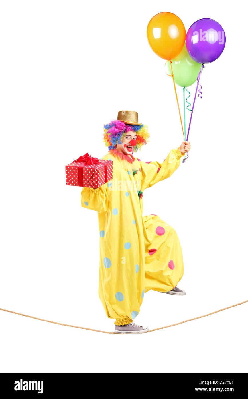 In voller Länge Portrait eines glücklichen männlichen Clown zu Fuß an einem Seil mit Haufen Luftballons und Gegenwart isoliert auf weißem Hintergrund Stockfoto