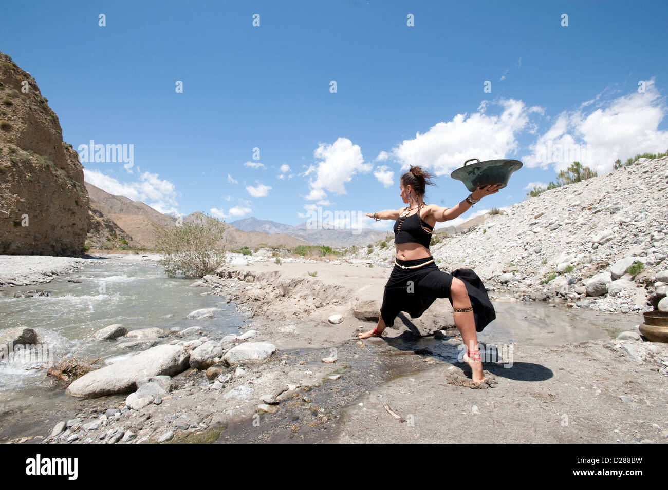 Dynamisches Bild einer Frau durch einen Fluss mit einer Schüssel. Stockfoto