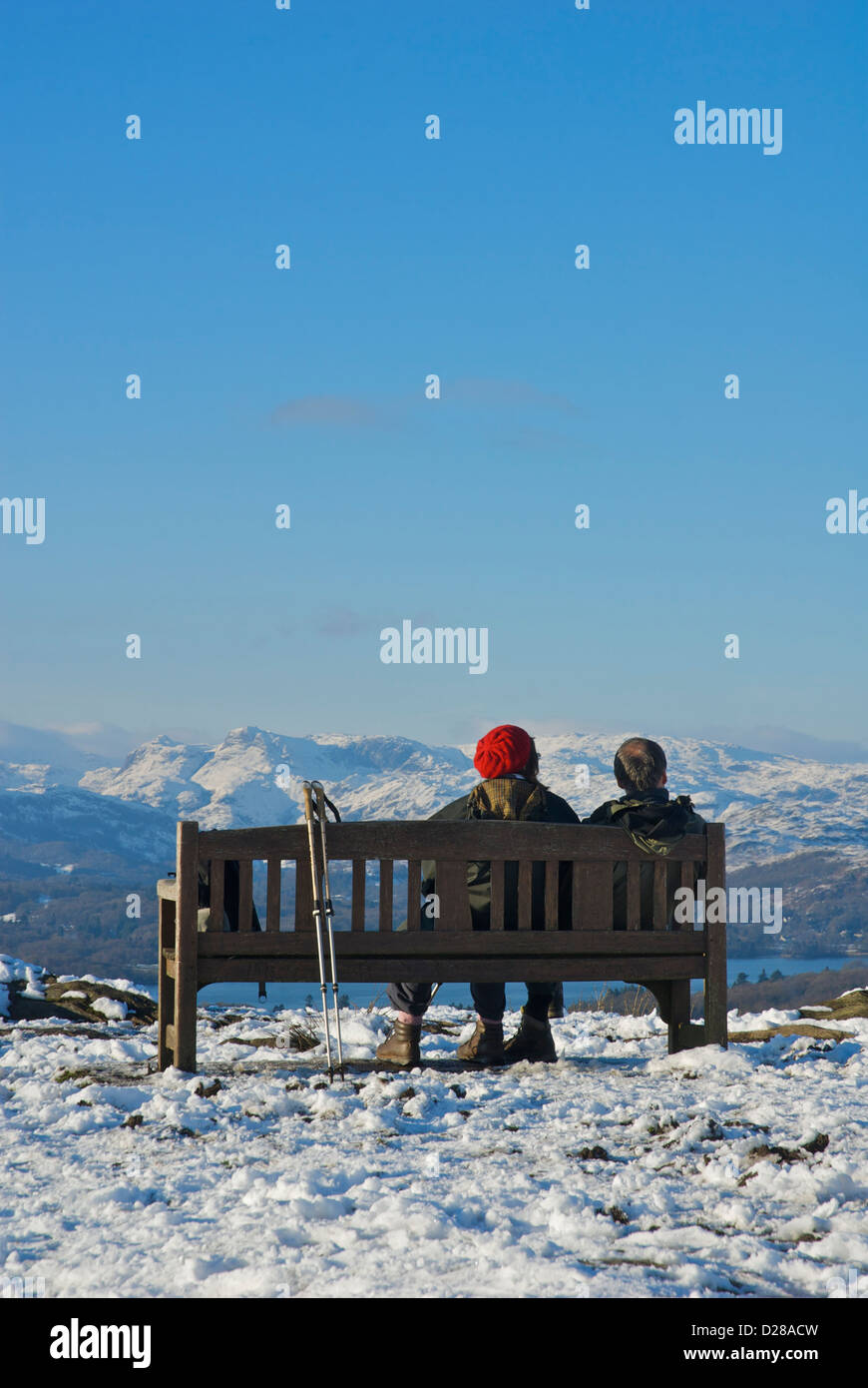 Zwei Wanderer sitzen auf einer Bank am Orrest Head mit Blick auf Lake Windermere und die Langdale Pikes, Cumbria, England UK Stockfoto