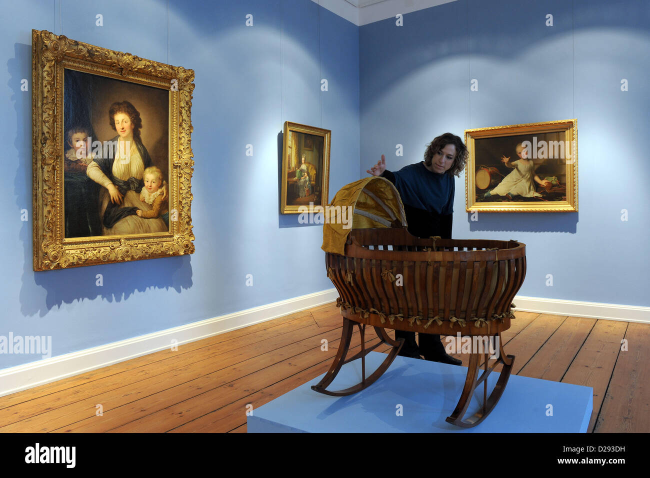 Ein Mitarbeiter sieht ein reiches Wiege (um 1820) im Museum Prinzenpalais in Oldenburg, Deutschland, 17. Januar 2013. Es ist Teil der Ausstellung "Kindheit. Kindheit von Renaissance bis moderne ", das vom 20 Januar bis zum 12. Mai stattfindet. Auf der Rückseite sind die Gemälde "Porträt von Christiane Schletter mit ihren drei Söhnen, 1795" von Anton Graff, "Frau im Zimmer mit Kind und Puppe, 1777" von Johann Heinrich Wilhelm Tischbein, und "Herzog Friedrich Emil August von Schleswig-Holstein-Sonderburg-Augustenburg, 1802" von Jens Juel gesehen. Foto: INGO WAGNER Stockfoto