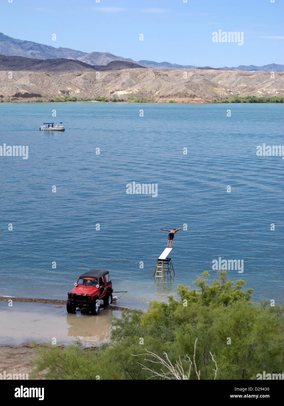 Mann ein Sprungbrett in Havasu See mit roten SUV Tauchen in Wasser am Rand des Sees und Ponton Boot im Hintergrund gedrängt Stockfoto