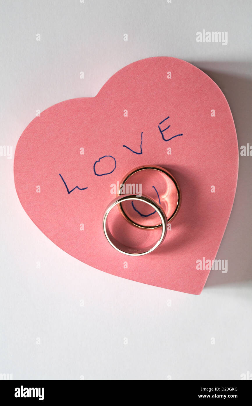 Botschaft der Liebe U geschrieben am Rosa herzförmige Post es pad mit zwei Trauringe isoliert auf weißem Hintergrund Stockfoto