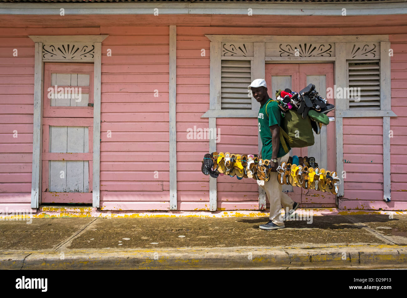 Verkauf von Schuhen Mann geht vorbei an Rosa Häuschen in Otra Banda, Provinz La Altagracia, Dominikanische Republik Stockfoto